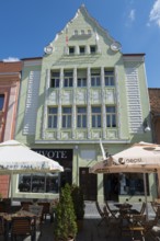 Historic Art Nouveau building in pastel green with café on the ground floor under a blue sky, town