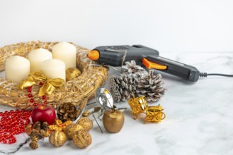 Craft scene with Advent wreath, white candles, decoration material and a glue gun on a marble