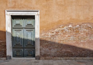 Red house facade with large green door, peeling plaster on brick wall, Venice, Veneto, Italy,