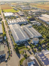 An industrial area with several buildings, roads and solar modules, surrounded by fields, taken