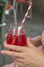 Women's hands holding a fruity bitter aperitif with raspberries in a glass with a straw, Franconia,