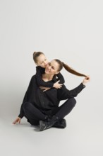 Little daughter hugs mother sitting on the floor, who pulled her ponytail aside. Modern family