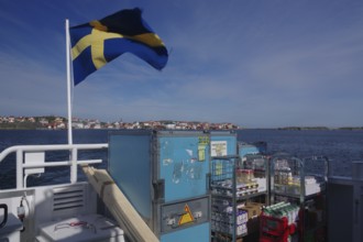 Ferry on the sea with Swedish flag, containers and view of a distant city. Clear blue sky and