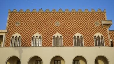 A historic building with a red and white pattern and battlements on the roof, harbour area, Rhodes