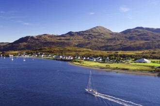 Sailboat on the sea next to a village and rolling hills under a blue sky, autumn, October,