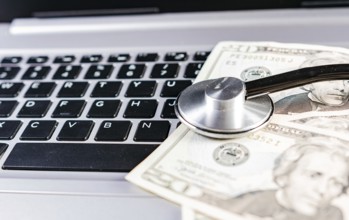 Medical cost concept. Stethoscope on top of money on laptop keyboard. Stethoscope on dollar bills