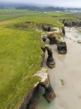 Steep cliffs with several prominent rock arches and lush green meadows reaching down to the sea,