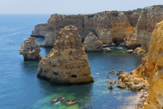 Several kayaks sail along imposing rocks rising from the clear blue sea, Praia da Marinha, Lagoa,