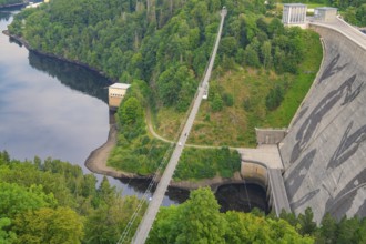 View of a bridge crossing a dam surrounded by dense forest and a calm body of water,