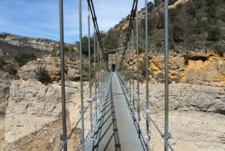 A long suspension bridge spans a deep, rocky gorge in a nature reserve, Noguera Ribagorçana