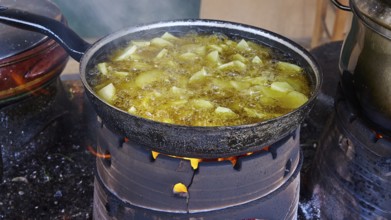 A pan of unpeeled potatoes roasting over an open fire, surrounded by steam, Slowfood Restaurant