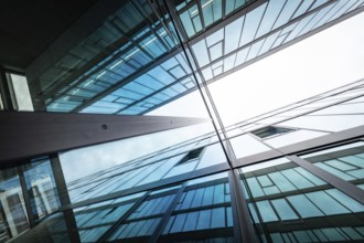 Mirrored glass facades of modern buildings reach up into the sky, reflecting blue and white,