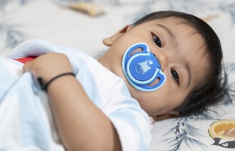 Baby boy playing lying on bed with pacifier on mouth