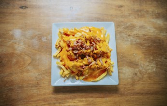 Top view of french fries covered with cheddar cheese and bacon on wooden table. French fries dipped