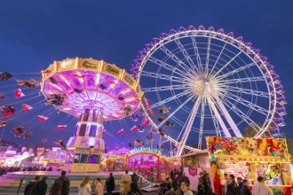 A lively funfair at dusk, illuminated by a large Ferris wheel and a colourful chain carousel,