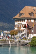 Beach hotel on the shore with people, mountains and autumn landscape in the background, Lake