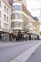 Horse-drawn carriage travelling through an urban street with historic buildings, Lake Brienz,