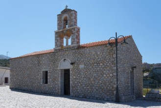 Historic stone church with bell tower and red roof under a blue sky in a Mediterranean setting,