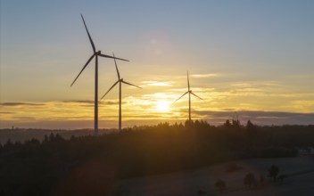 Wind turbines at sunrise, surrounded by trees and a peaceful landscape, Rems Valley,