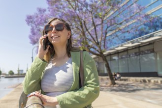 Businesswoman using smartphone near blooming jacaranda mimosifolia tree, enjoying sunny day in