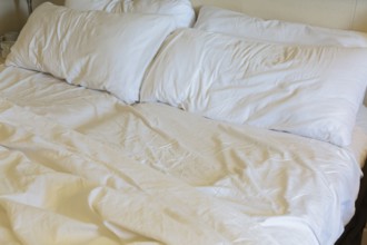 Close-up of rippled and creased white cotton bed sheets and pillows on unmade king size bed, La