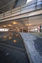 Puddle of water reflects the interior of a multi-storey car park with steel structure, Kaufland