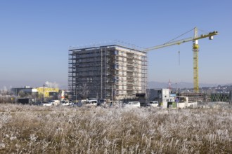 Large building under construction with crane, surrounded by frost-covered fields, residential