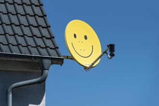 Funny satellite dish, yellow with smiley, satellite antenna on the roof of a house, satellite