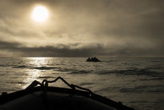 Inflatable boats, tourists, sun behind clouds, Kvitøya, Svalbard and Jan Mayen archipelago, Norway,