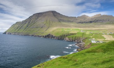 Green coastal landscape with mountains and houses under a blue sky, Vidareidi, Vidoy Island,