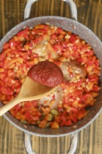 Adding a tomato paste to a pot with chopped red and green bell peppers, onions, and seasonings