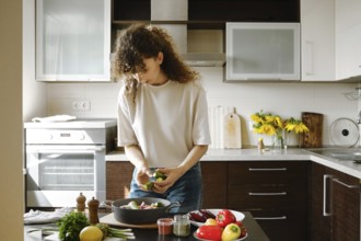 Woman adding fresh zucchini to a pan with vegetables for baking in the oven