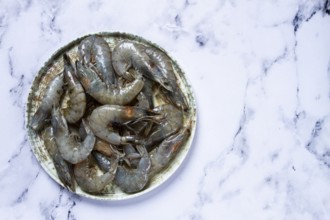 Fresh shrimp, laid out on a round plate, on a marble background, ready for grilling, seafood,