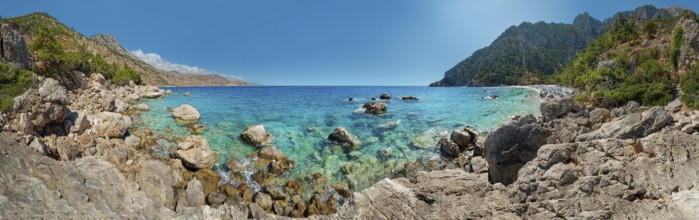 Clear, turquoise-coloured sea at Apella beach with rocks along the coast and mountains in the