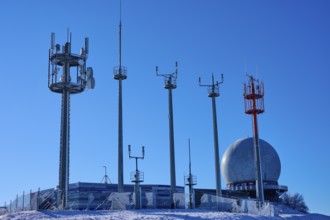 Several transmission masts and a radar station Radom in clear weather with snow and blue sky,