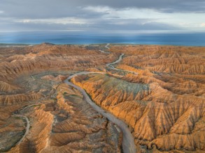 River bed runs through a landscape of eroded hills, badlands, Issyk Kul Lake in the background,