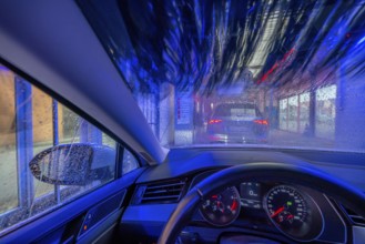 Car in an automatic car wash, car wash tunnel, cleaning foam is sprayed on, rotating brushes clean