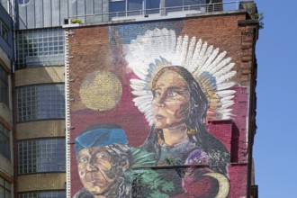 A mural shows a woman with feather jewellery and a man in front of a building, Mural Trail,