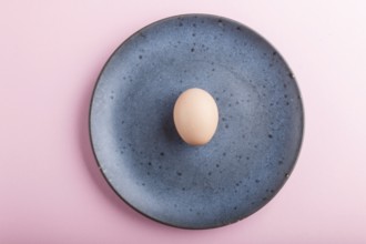 Raw uncooked single egg on a blue ceramic plate on a pink pastel background. top view, copy space