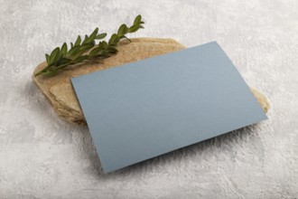 Blue paper business card, mockup with natural stone and boxwood branch on gray concrete background.