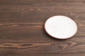 Empty white with dots ceramic plate on brown wooden background. Side view, copy space