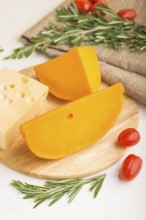 Various types of cheese with rosemary and tomatoes on wooden board on a white wooden background and