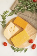 Various types of cheese with rosemary and tomatoes on wooden board on a white wooden background and