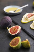 Summer appetizer with pear, cottage cheese, figs and honey on slate board on a black concrete