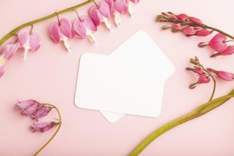 White business card with pink dicentra, broken heart flowers on pink pastel background. top view,