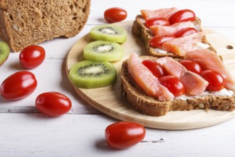 Smoked salmon sandwiches with butter and cherry tomatoes on white wooden background. close up