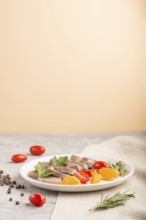 Boiled pork tongue with tomatoes and herbs on a gray and orange background and linen textile. Side