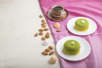 Green mousse cake with pistachio cream and a cup of coffee on a white wooden background and pink