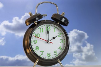 Symbolic image of the time change to summer time: close-up of an alarm clock in front of a blue sky