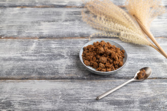 Plate with unrefined brown cane sugar on gray wooden background. side view, copy space